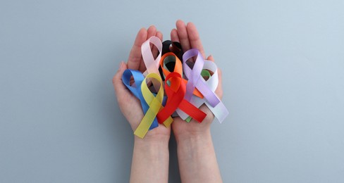 Photo of Woman with many colorful awareness ribbons on grey background, top view