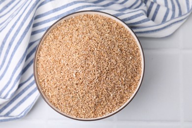 Photo of Dry wheat groats in bowl on white tiled table, top view