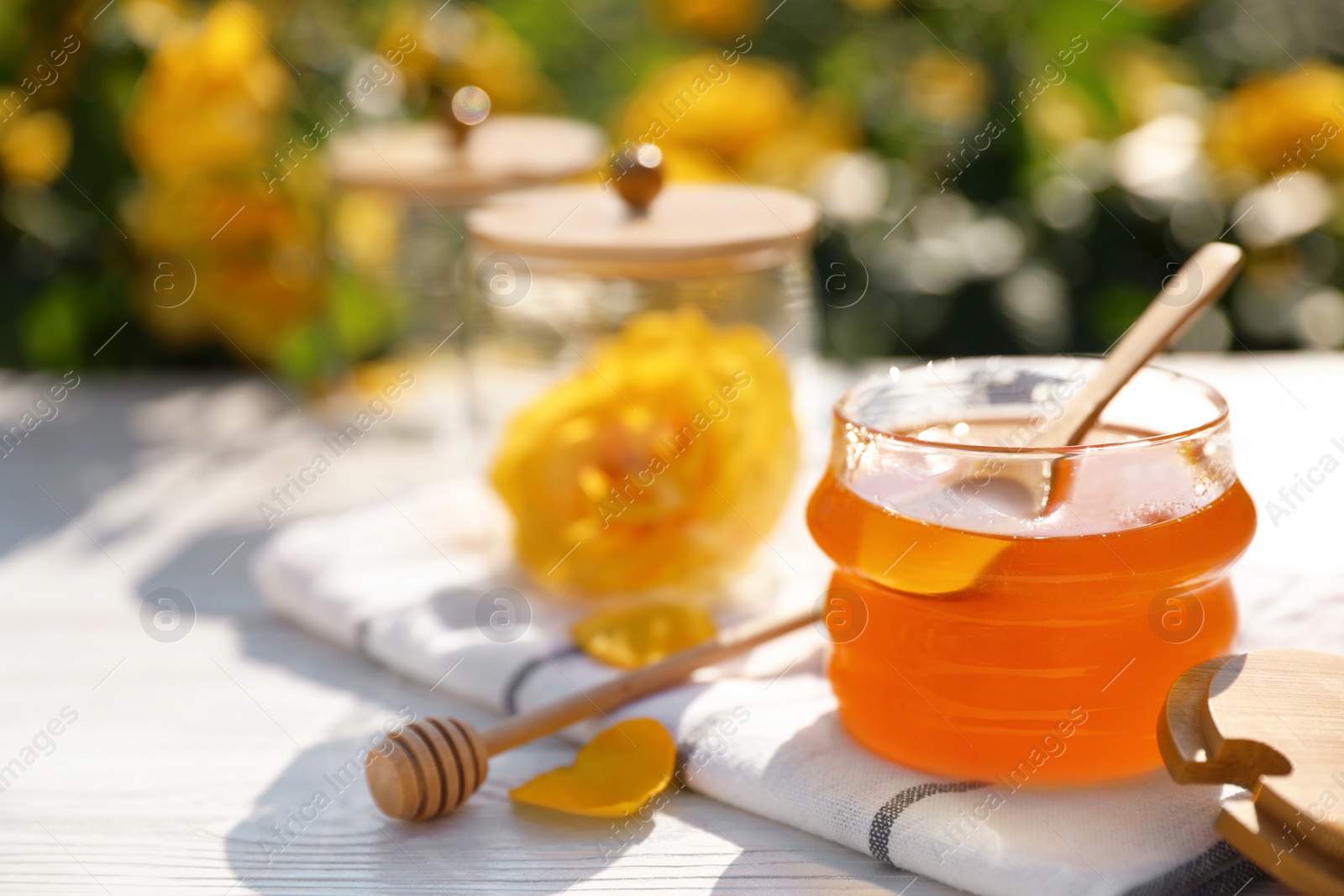 Photo of Jar with fresh rose honey on white wooden table outdoors. Space for text