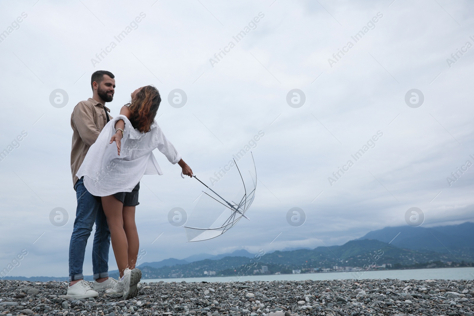 Photo of Young couple with umbrella enjoying time together under rain on beach, space for text