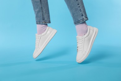 Photo of Woman wearing stylish white sneakers on light blue background, closeup