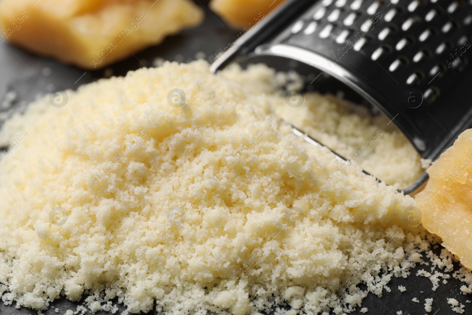 Photo of Pile of grated parmesan cheese and grater on black table, closeup