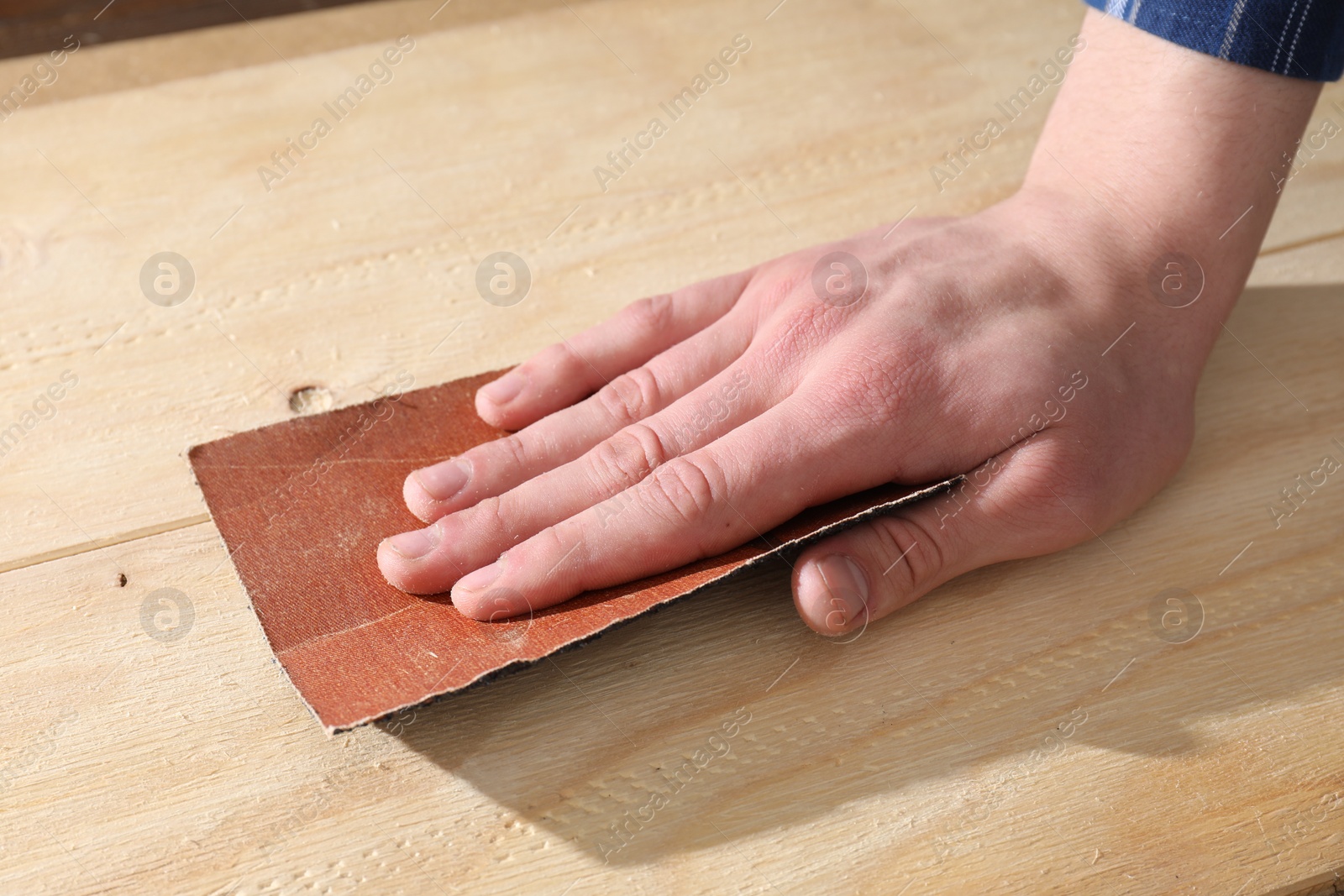 Photo of Man polishing wooden planks with sandpaper, closeup