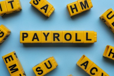 Word Payroll made with yellow cubes on light blue background, flat lay