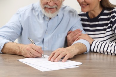 Happy senior couple signing Last Will and Testament at wooden table, closeup