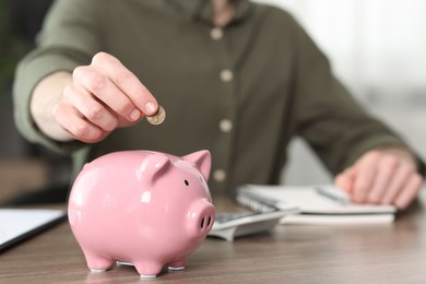 Photo of Financial savings. Man putting coin into piggy bank at wooden table, closeup