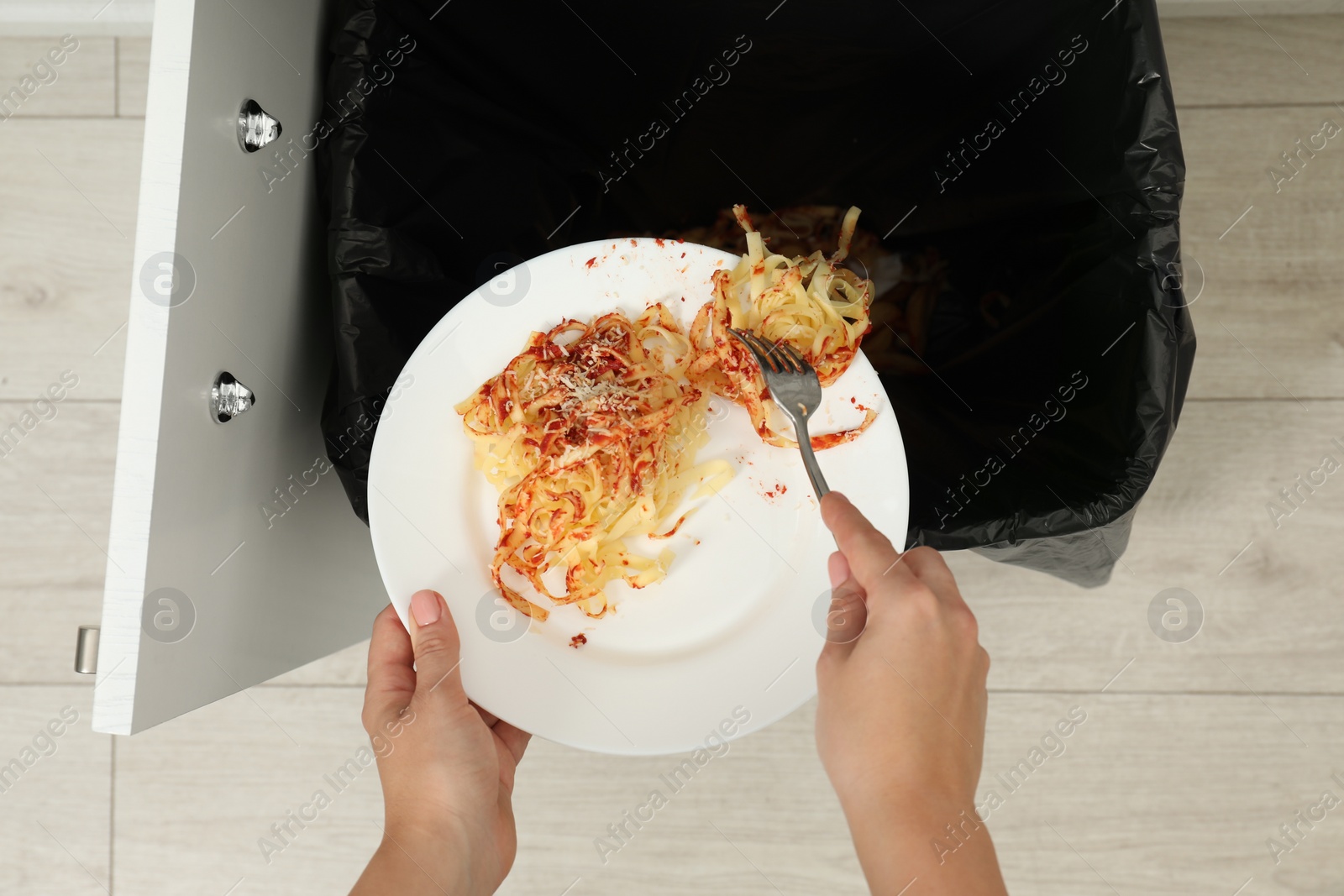 Photo of Woman throwing pasta into bin indoors, top view