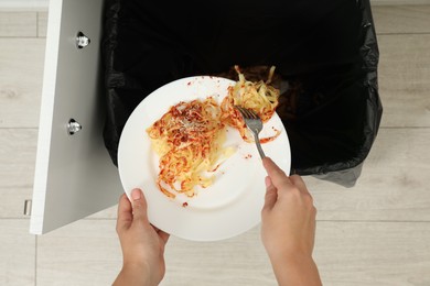 Woman throwing pasta into bin indoors, top view