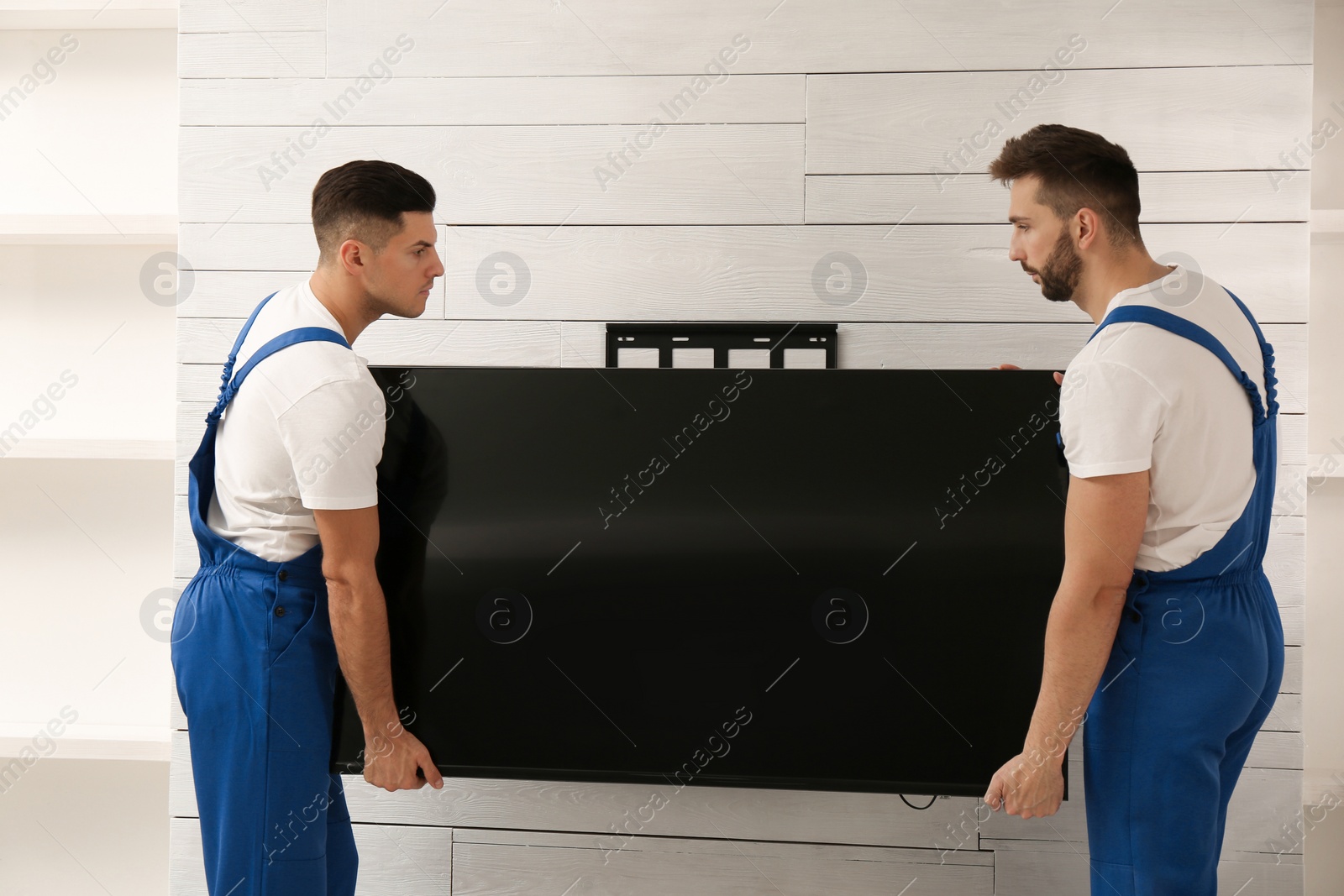 Photo of Professional technicians installing modern flat screen TV on wall indoors