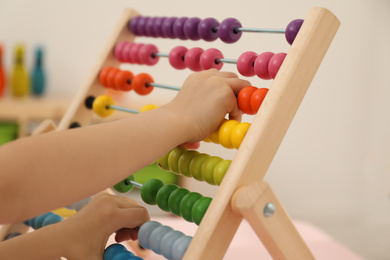 Cute child playing with wooden abacus at table in room, closeup