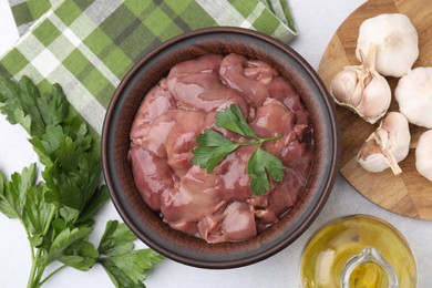 Photo of Bowl with raw chicken liver, parsley and garlic on white table, flat lay