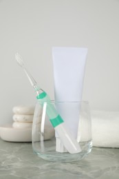 Photo of Electric toothbrush in glass and tube with paste on light grey marble table