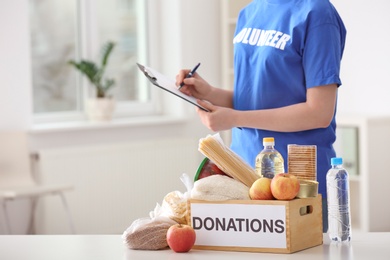 Photo of Female volunteer listing food products from donation box indoors