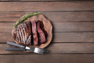 Photo of Delicious grilled beef meat and rosemary served on wooden table, top view. Space for text