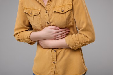 Photo of Young woman suffering from stomach pain on grey background, closeup