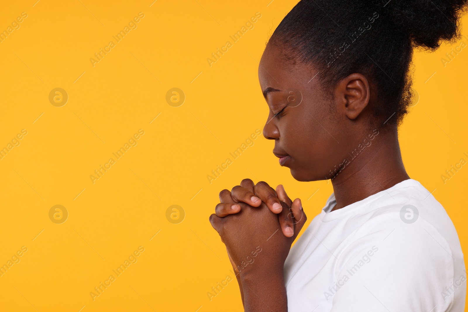 Photo of Woman with clasped hands praying to God on orange background. Space for text