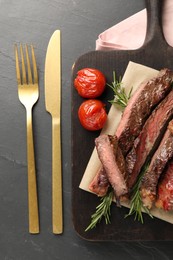 Photo of Delicious grilled beef with vegetables and rosemary served on dark gray table, flat lay