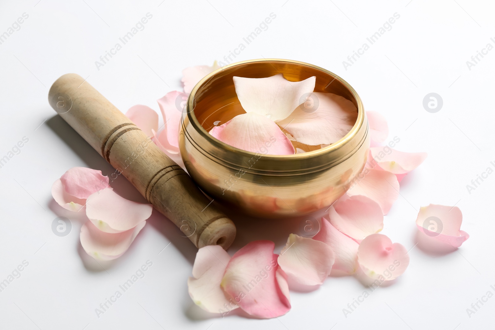 Photo of Golden singing bowl with petals and mallet on white background. Sound healing