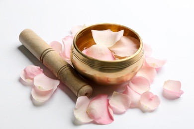 Photo of Golden singing bowl with petals and mallet on white background. Sound healing