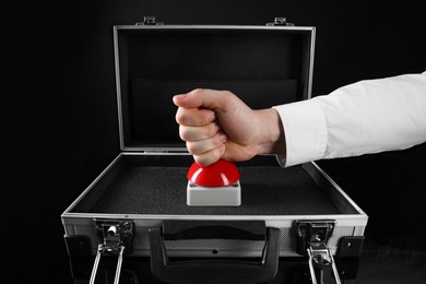 Man pressing red button of nuclear weapon on black background, closeup. War concept