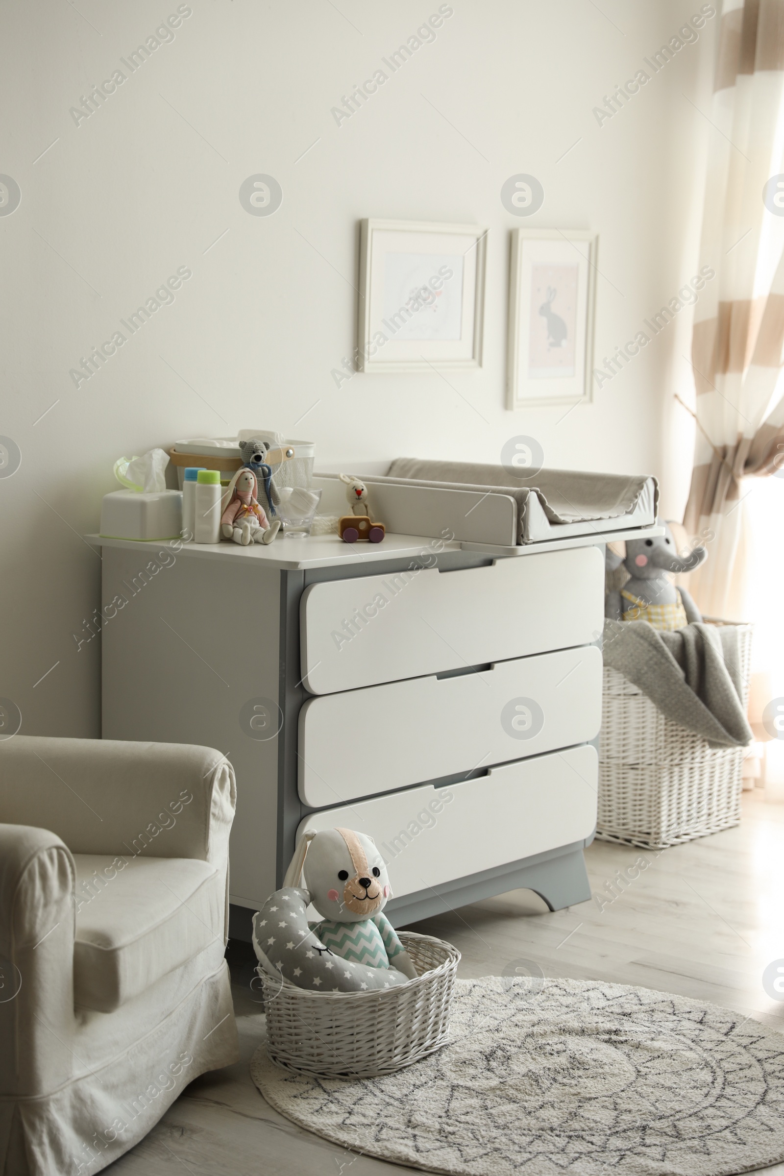 Photo of Beautiful baby room interior with toys, armchair and modern changing table