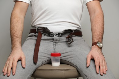 Donor with unzipped pants and container of sperm sitting on stool against beige background, closeup