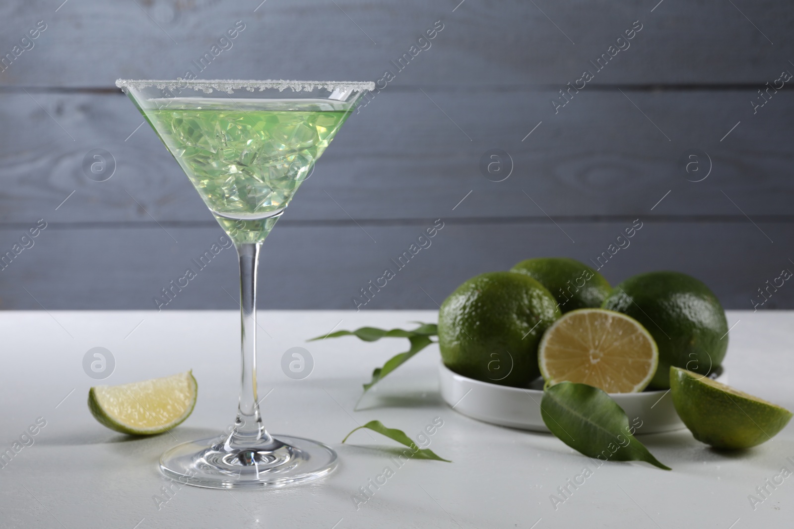 Photo of Delicious Margarita cocktail with ice cubes in glass and lime on white table