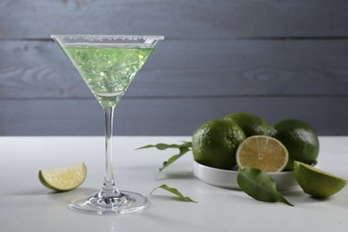 Delicious Margarita cocktail with ice cubes in glass and lime on white table