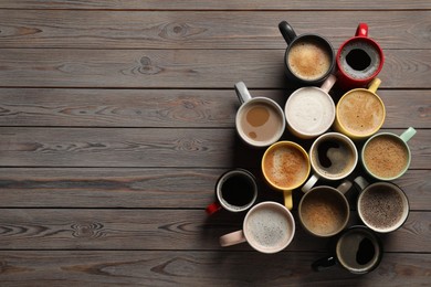 Photo of Many different cups with aromatic coffee on wooden table, flat lay. Space for text