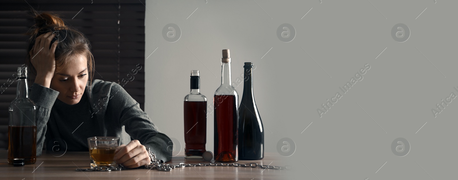 Image of Suffering from hangover. Woman chained with glass of liquor at table indoors, space for text. Banner design