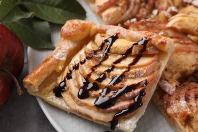 Photo of Piece of tasty apple pie with chocolate topping, fresh fruit and green leaves on table, closeup