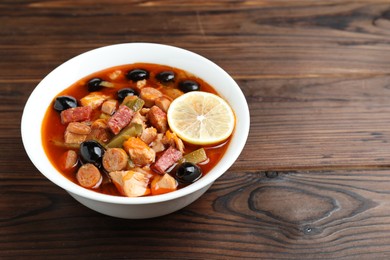 Meat solyanka soup with sausages, olives and vegetables on wooden table, space for text