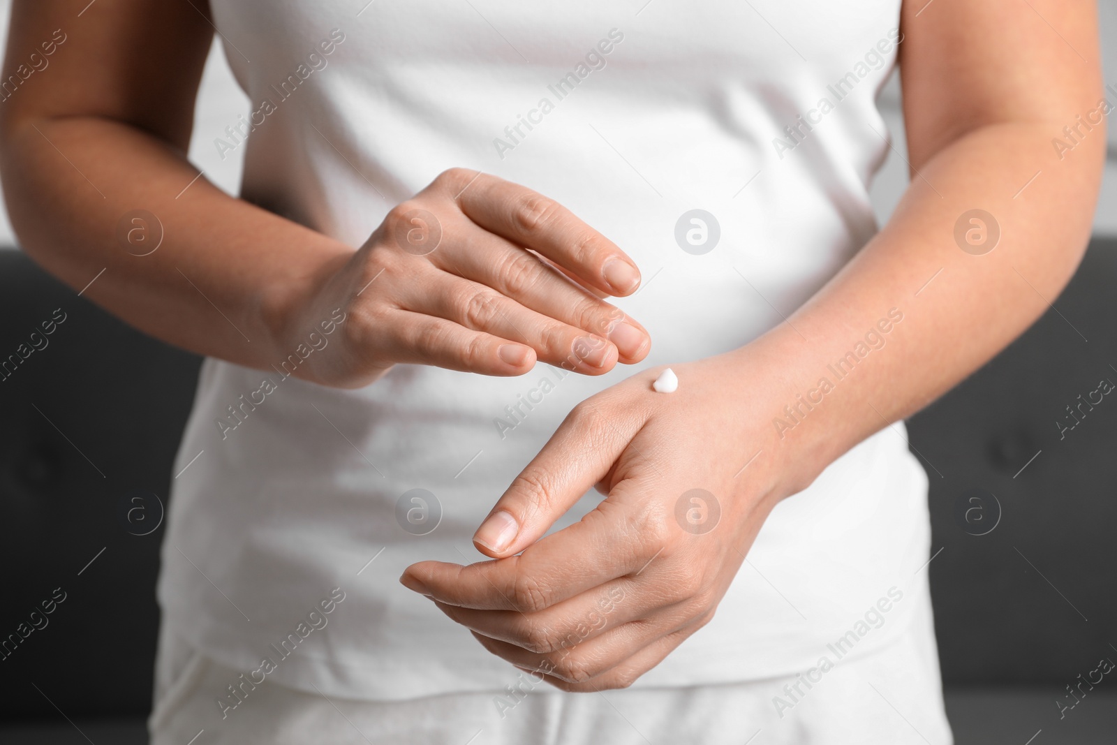 Photo of Woman applying cosmetic cream onto hand on blurred background, closeup