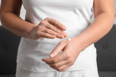 Photo of Woman applying cosmetic cream onto hand on blurred background, closeup