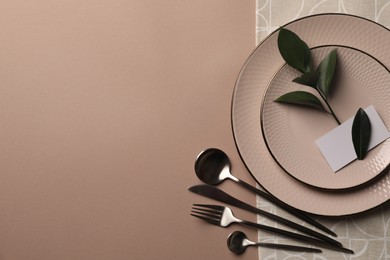 Photo of Stylish table setting. Plates, cutlery, blank card and green twig on beige background, top view with space for text