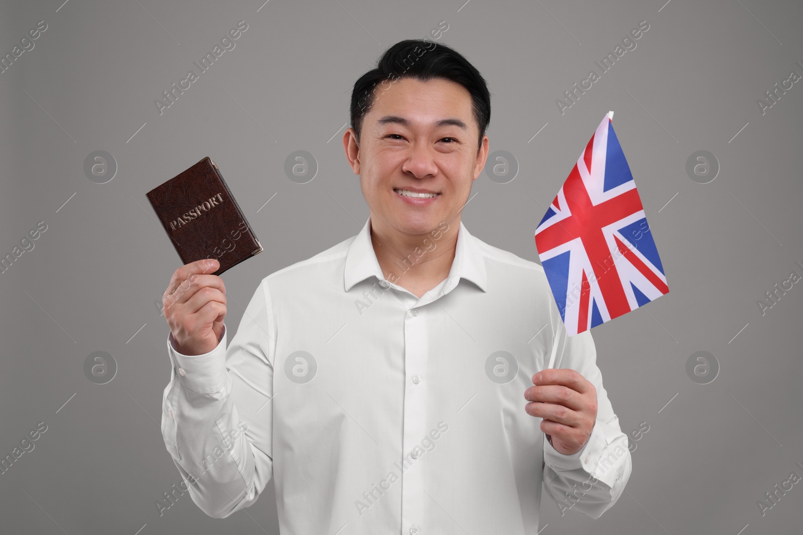 Photo of Immigration. Happy man with passport and flag of United Kingdom on grey background