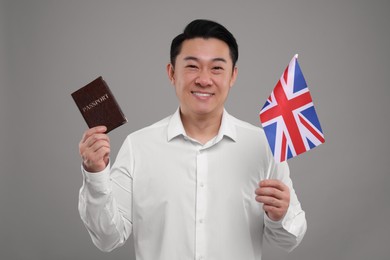 Photo of Immigration. Happy man with passport and flag of United Kingdom on grey background