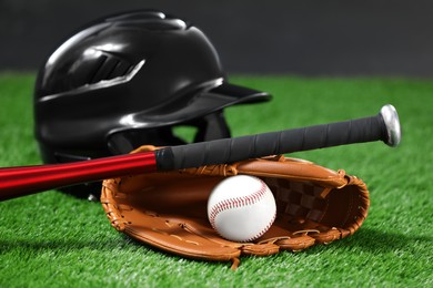 Photo of Baseball bat, batting helmet, leather glove and ball on green grass against dark background, closeup