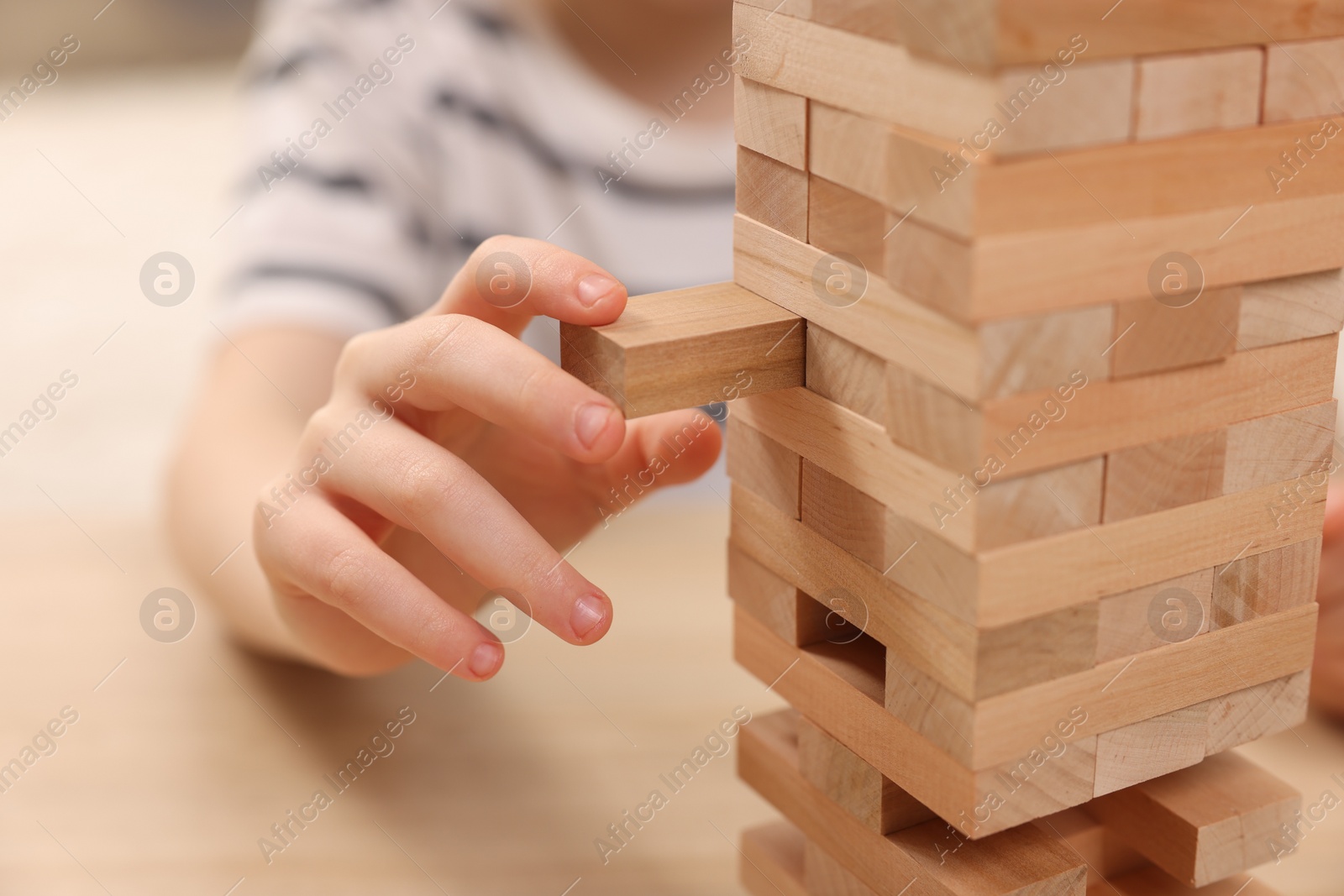 Photo of Child playing Jenga at table indoors, closeup