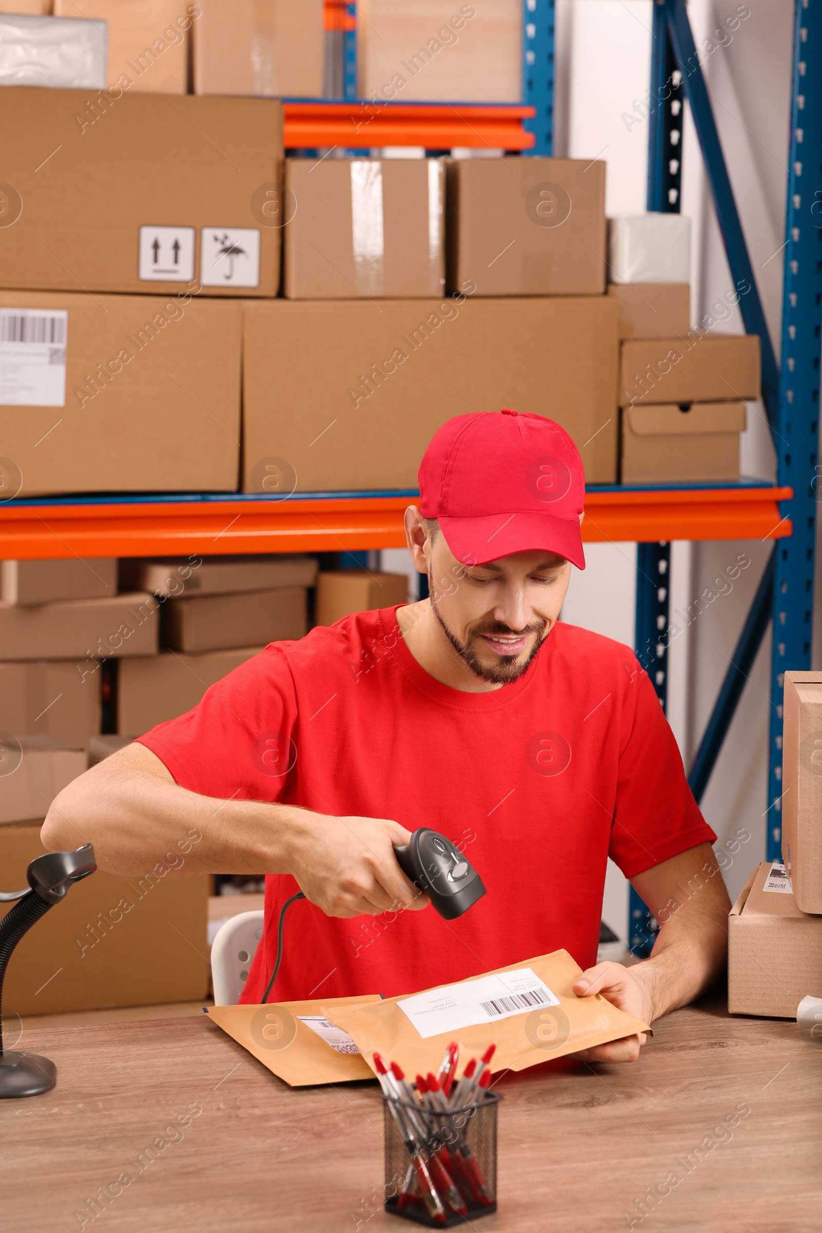 Photo of Post office worker with scanner reading parcel barcode at counter indoors