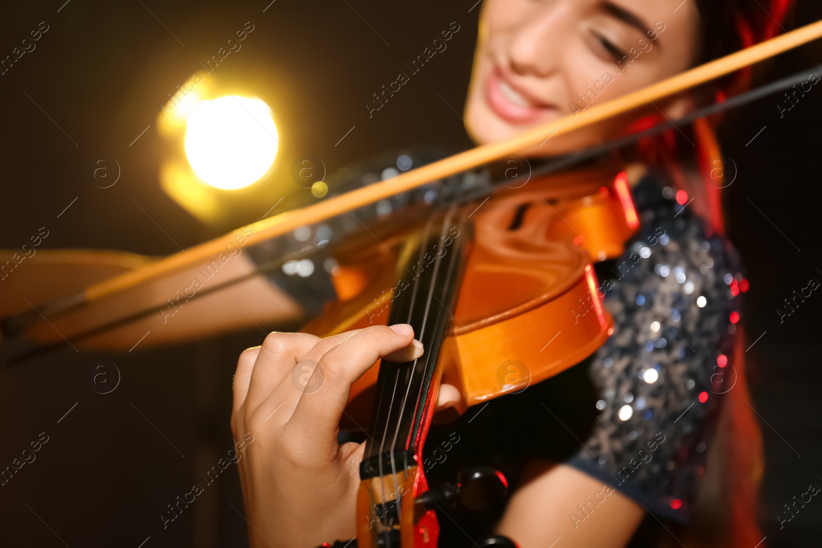 Photo of Beautiful young woman playing violin in dark room, closeup