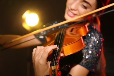 Beautiful young woman playing violin in dark room, closeup