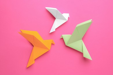 Photo of Beautiful colorful origami birds on pink background, flat lay