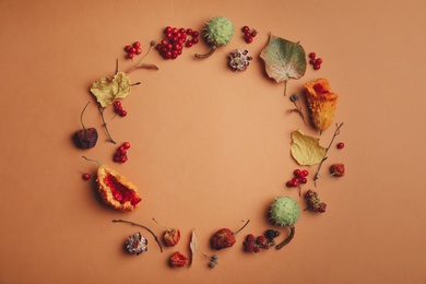Photo of Dried flowers, leaves and berries arranged in shape of wreath on brown background, flat lay with space for text. Autumnal aesthetic