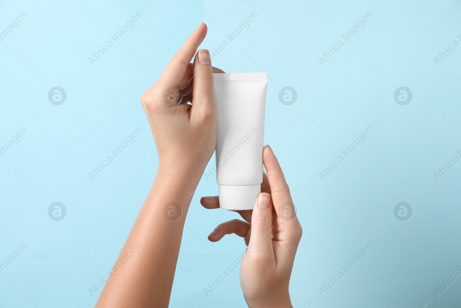 Photo of Woman with tube of hand cream on light blue background, closeup