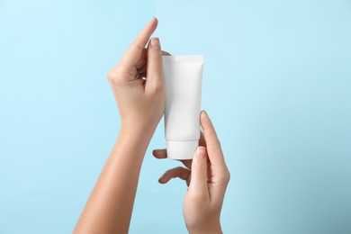 Woman with tube of hand cream on light blue background, closeup