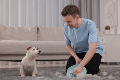 Photo of Smiling man with brush and pan removing pet hair from carpet at home