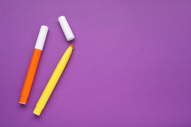 Photo of Orange and yellow markers on purple background, flat lay. Space for text