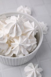 Photo of Tasty meringue cookies in bowl on white tiled table, closeup