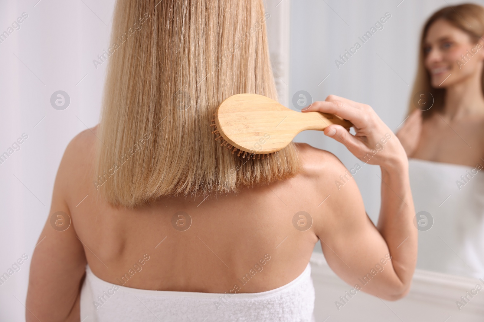 Photo of Woman brushing her hair near mirror in room, back view